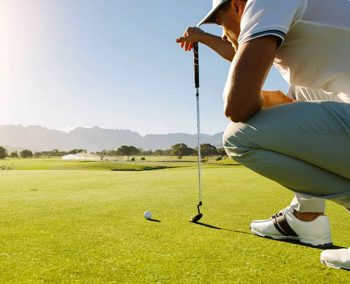 Golfer lining up a putt on a sunny golf course green with mountains in the background